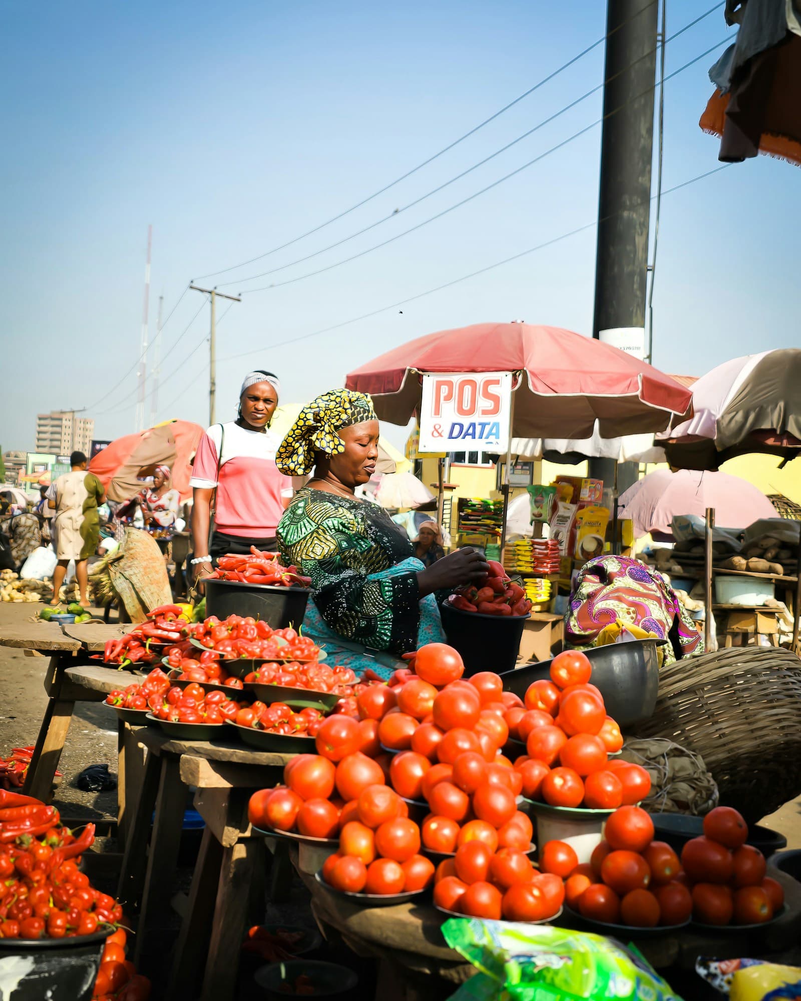A trader arranging tomatoes and peppers at her market stall